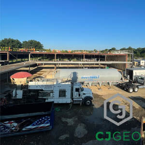 A CJGEO bulk grouting truck parked at a job site in front of a large silver bulk material storage tanker.