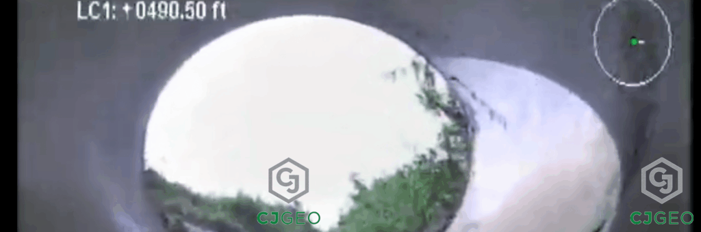 photo taken by a remote video crawler camera looking upstream out of a large concrete stormwater pipe, with the stream bank and sky in the background
