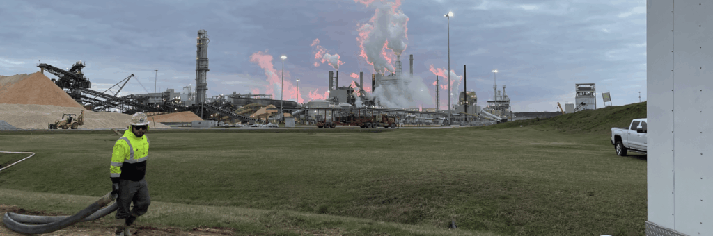 A CJGeo worker pulling a rose through a field with a paper mill in the background during sunset.