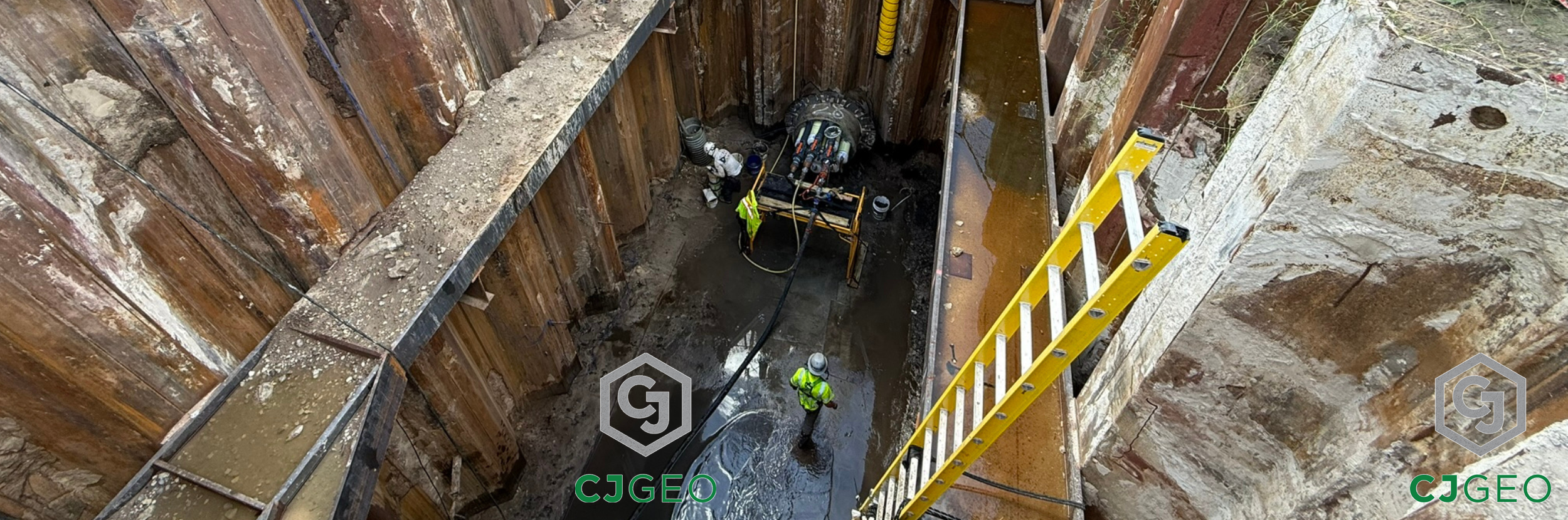 two CJGeo workers at the base of a sheet pile shaft with a microtunnel containing electrical conduits in preparation for thermal grouting operations.