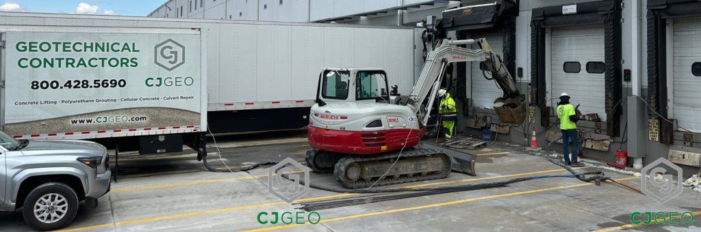 a grouting truck, mini excavator, sonic drill and workers adjacent to a warehouse loading dock
