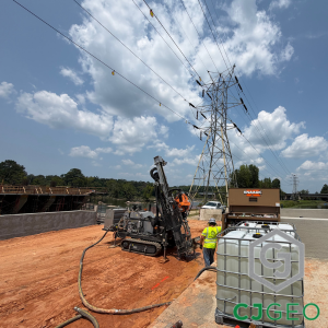 An IBC tote of water sitting next to a sonic drill working under powerlines. 