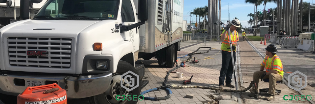 A CJGeo grouting truck sitting adjacent to a modular grade crossing with workers injecting polyurethane grout under the crossing panels.